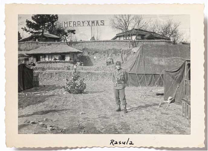 black white photo of a man standing in a field with Merry-XMas banner