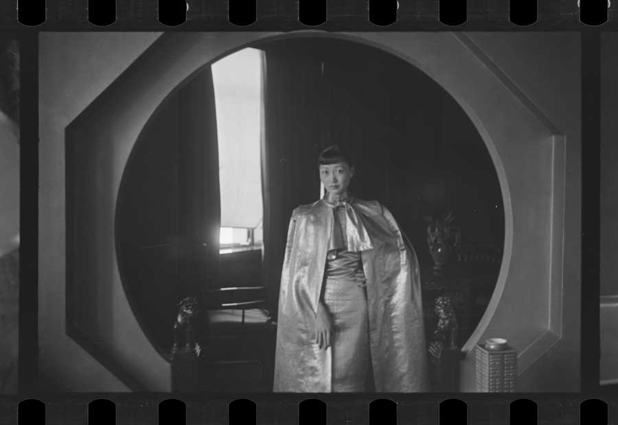 Anna May Wong posing for a portrait in front of a backdrop. Digitized black and white photo negatives.