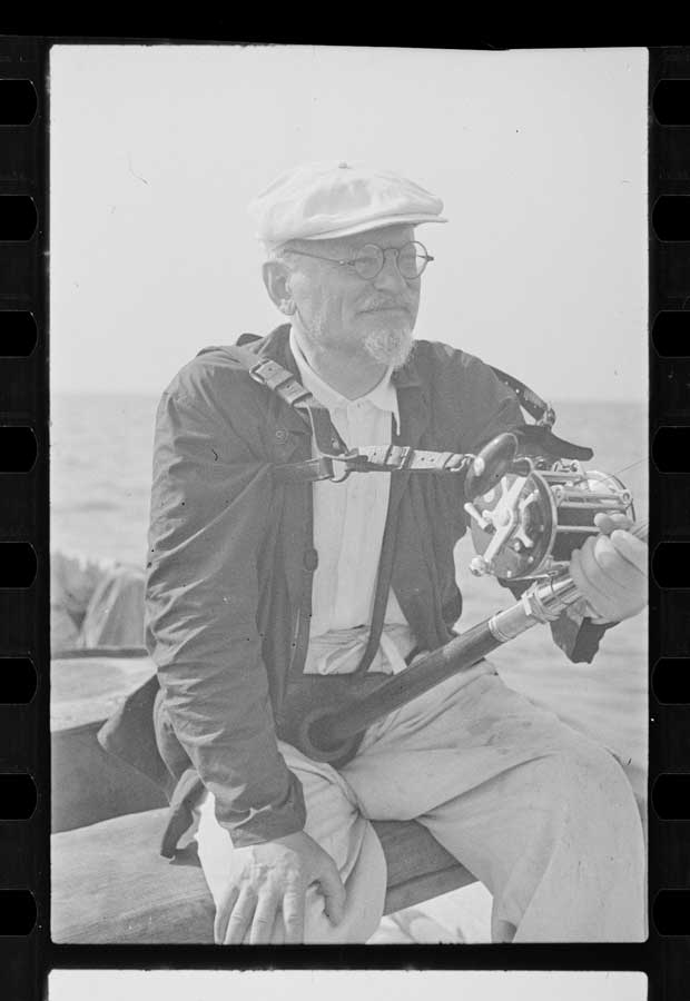 Leon Trotsky holding a fishing pole seated on a boat. Digitized black and white photo negatives.
