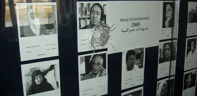 Detail of a photo of a diplaycase with a bullet hole in the glass, inside are black and white photographs of people with names and info.