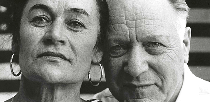 Detail of black and white photo of a woman and man in front of an American flag.