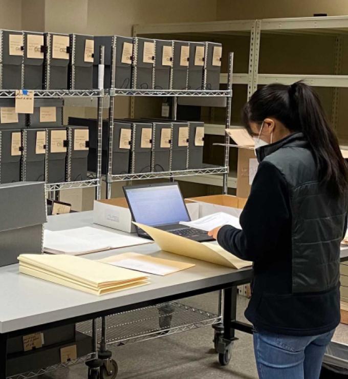Jessica Y standing in front of a table with documents, laptop, and manuscript boxes