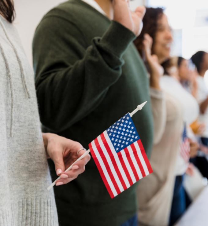 The group of multiracial people stand and raise their hand to say the pledge.