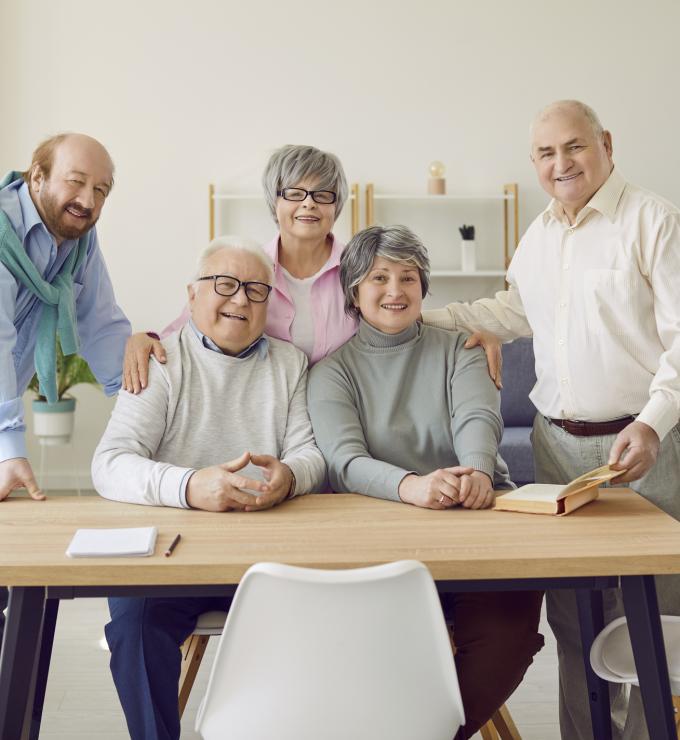Group of senior people men and women sitting in nursing home at the table and looking at camera. - stock photo