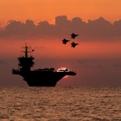 Aircraft carrier and fighters at sunset in the sea - stock photo