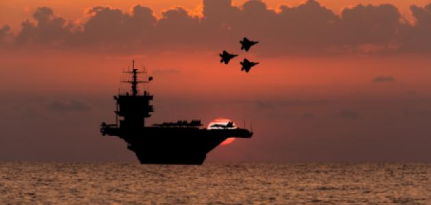 Aircraft carrier and fighters at sunset in the sea - stock photo