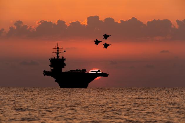 Aircraft carrier and fighters at sunset in the sea - stock photo