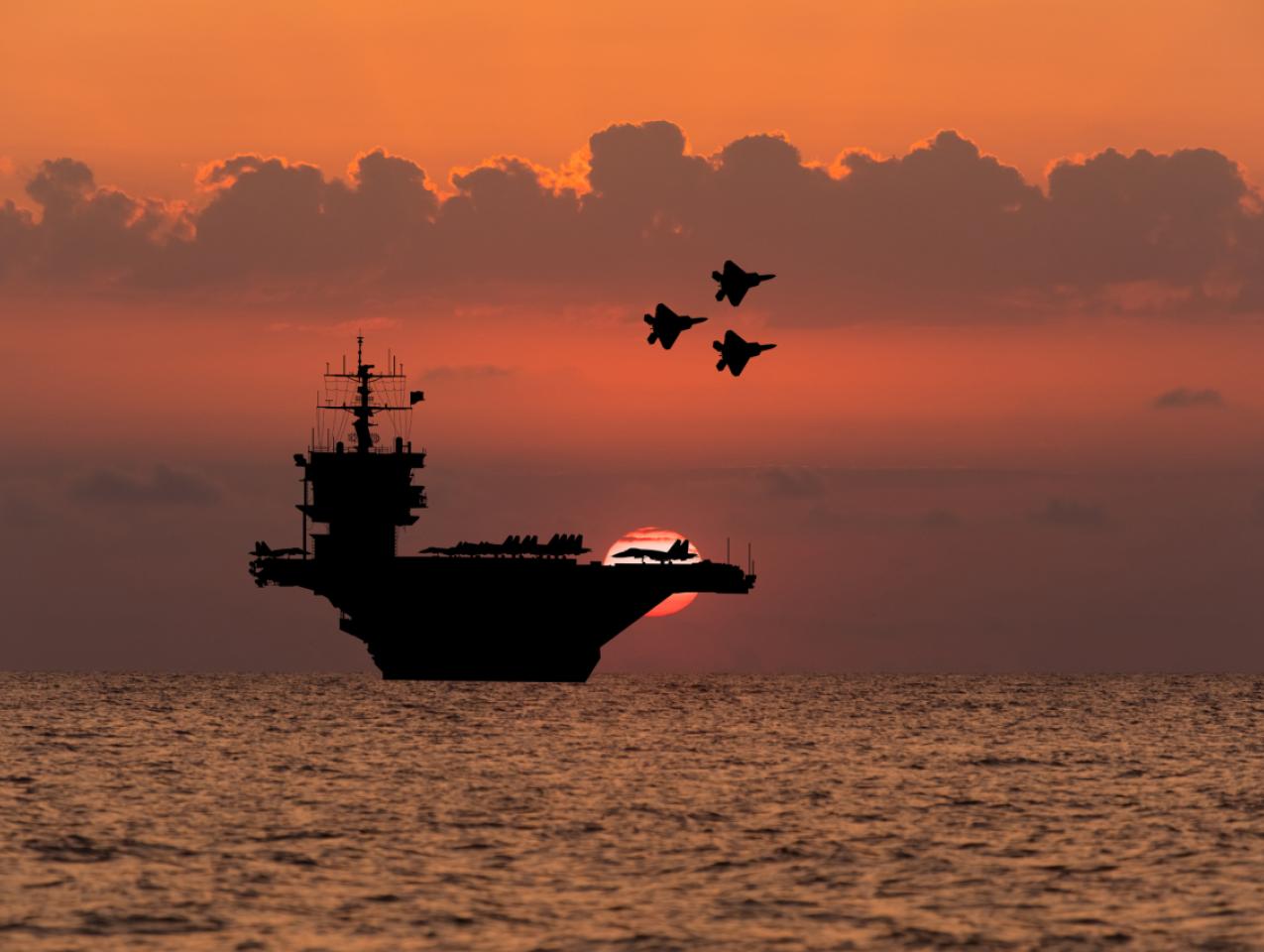 Aircraft carrier and fighters at sunset in the sea - stock photo